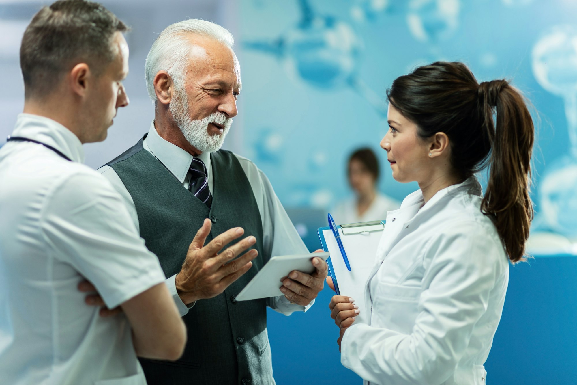 Senior businessman with touchpad communicating with doctors at hospital.